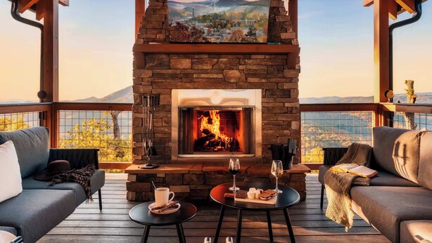 A cozy outdoor seating area with a stone fireplace, wooden furniture, and a scenic view of mountains. - Incredible 180 VIEWS! | Luxury Lodge | Indoor Pool (Sevierville)