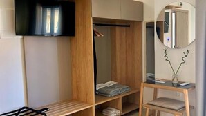 Una camera moderna con armadio a muro, una piccola scrivania e una TV montata a parete.