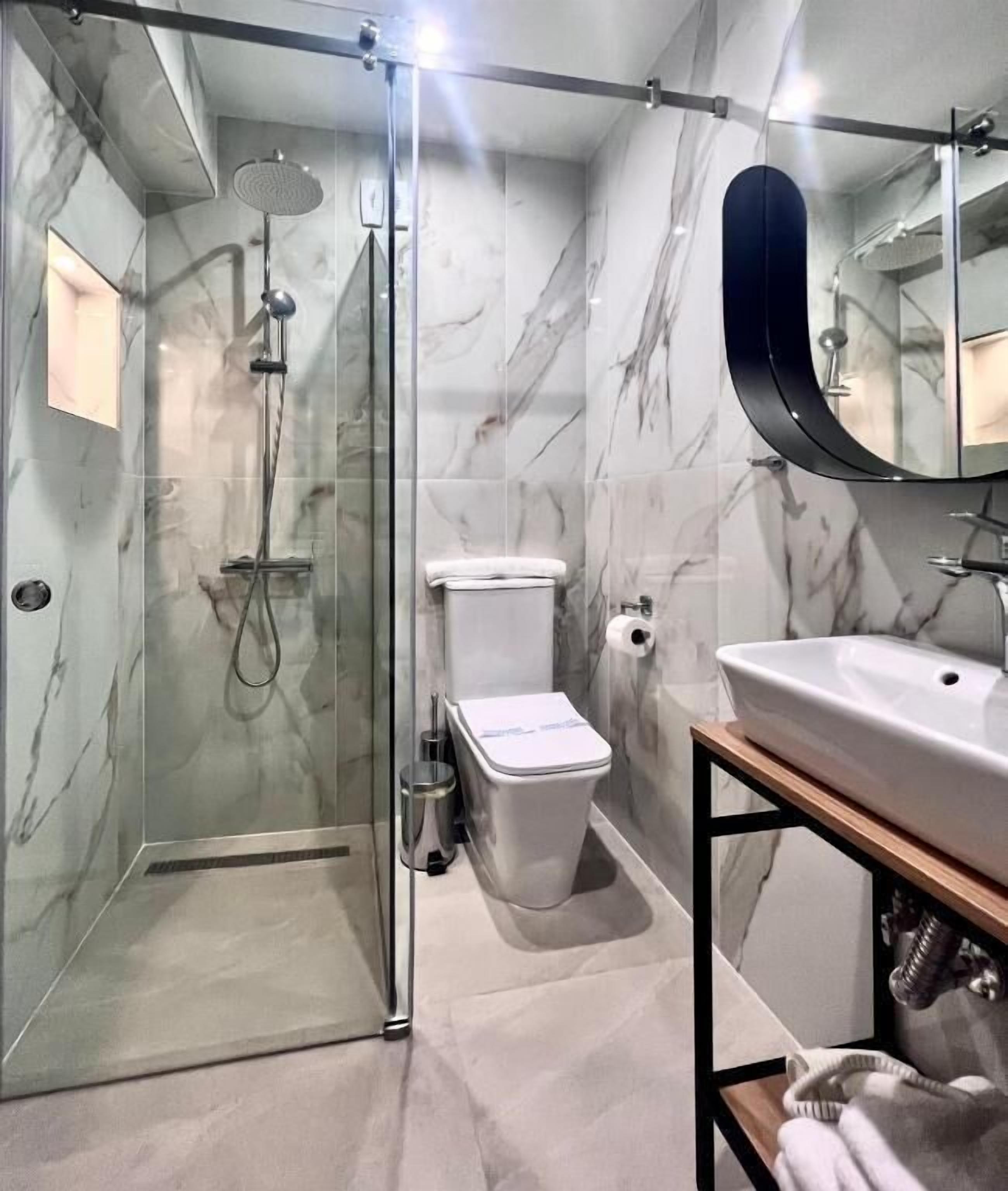 A modern bathroom with a glass-enclosed shower, a toilet, and a sink with a mirror above.