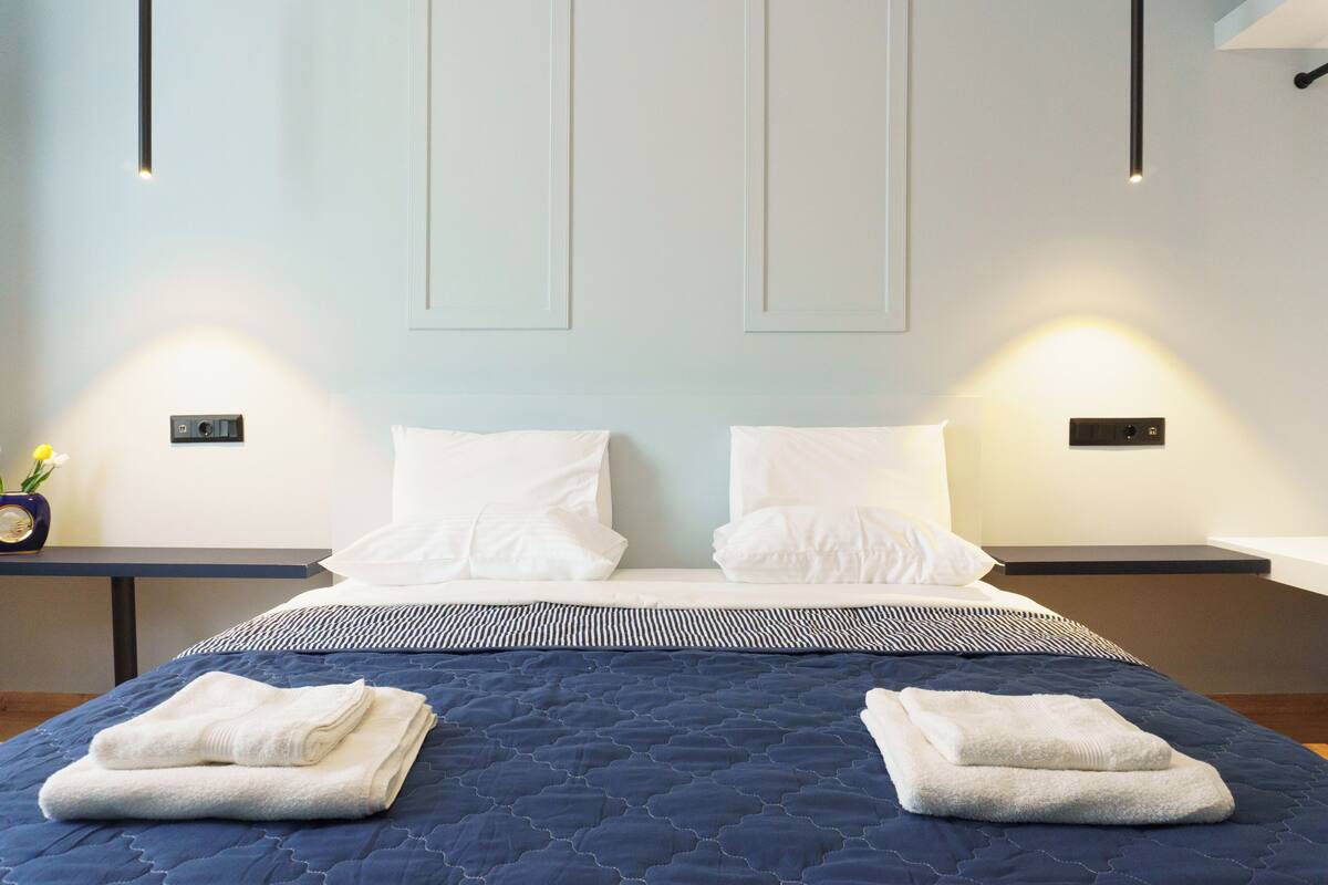 A hotel room with a large bed, two bedside tables, and a wall-mounted light fixture.