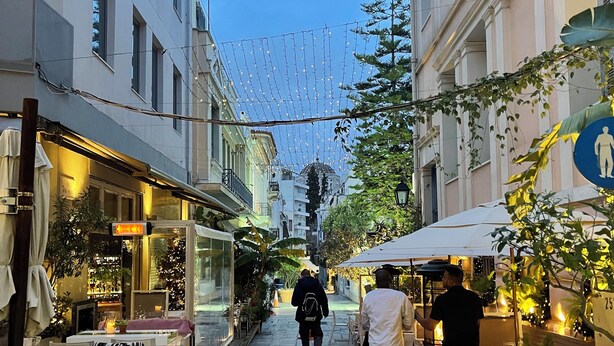 A narrow street with outdoor seating, buildings on either side, and string lights overhead. - Sani Deluxe Suite Home (Athens)