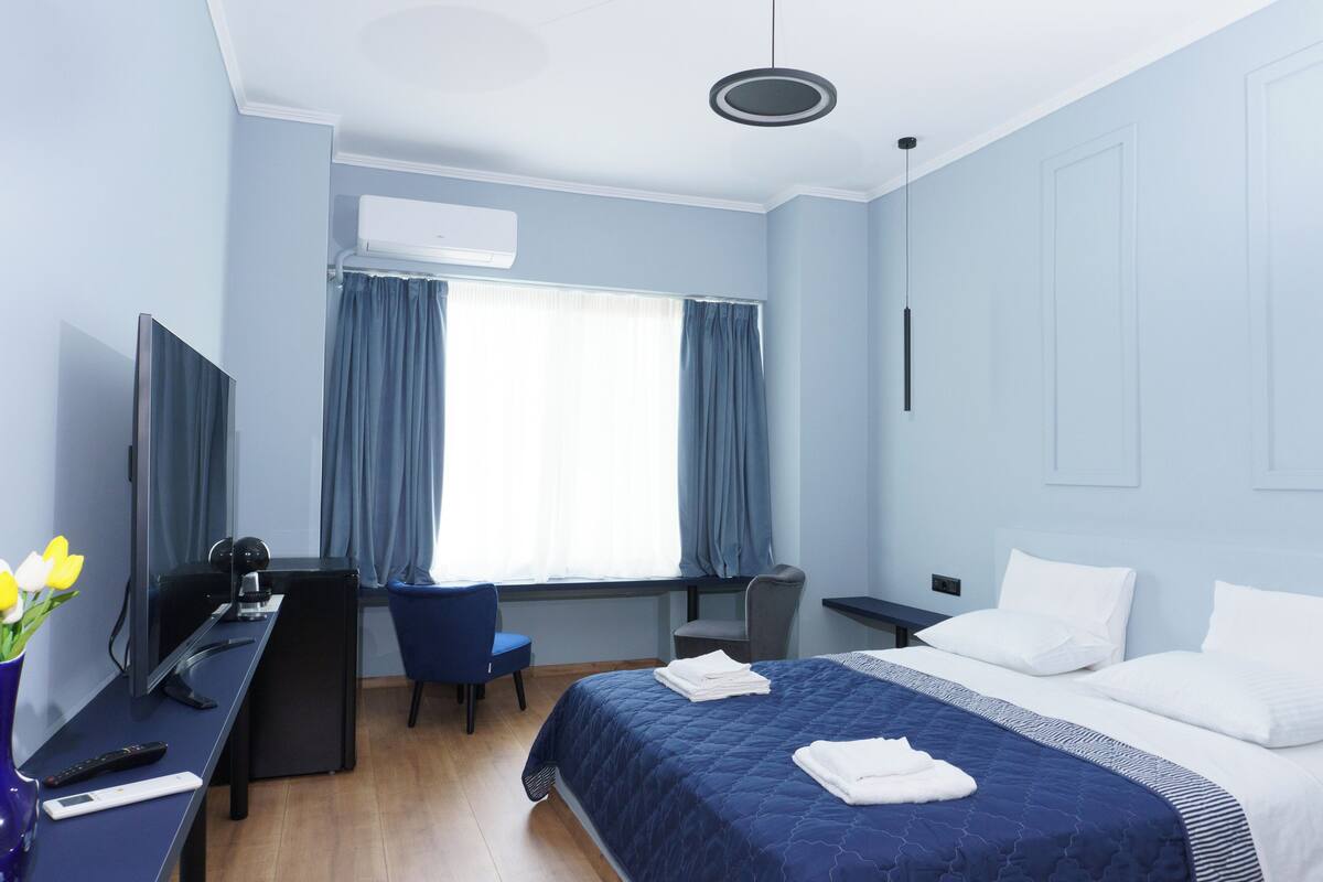 A hotel room with a bed, a desk, a chair, a TV, and a window with curtains.
