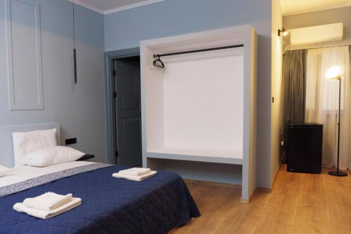 A hotel room with a bed, a desk, and a chair. There is a window with curtains and a wall-mounted air conditioner.