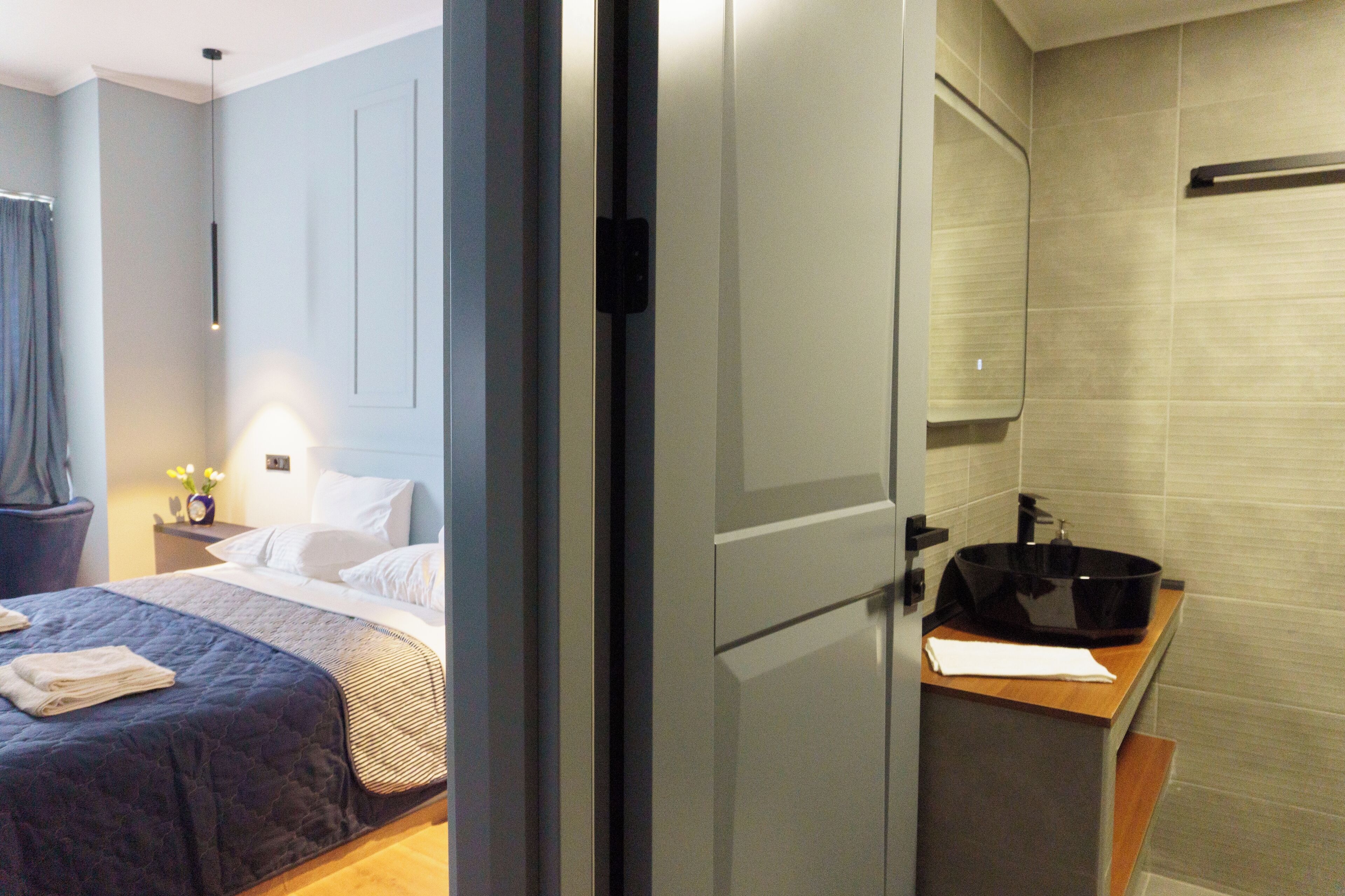 Quarto de hotel com cama, mesa de cabeceira e banheiro com pia e espelho.