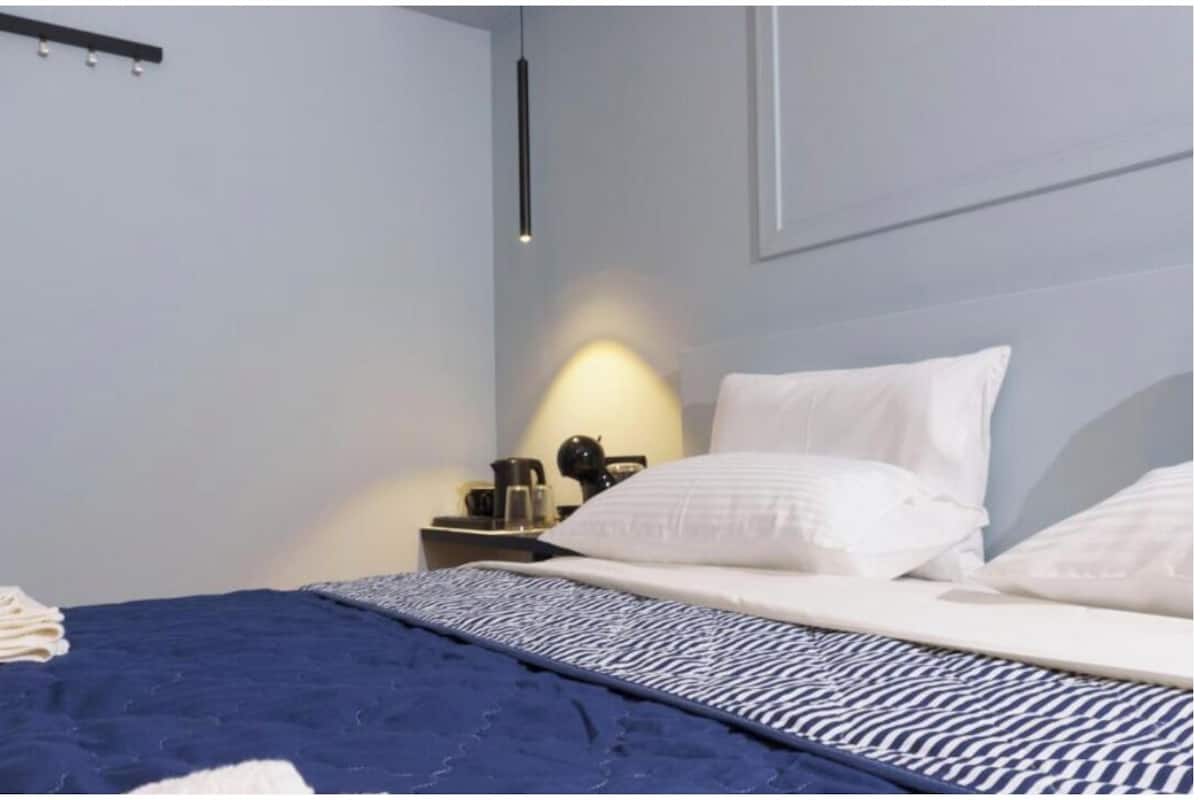 A neatly made bed with white and blue bedding, a bedside table with a lamp, and a wall-mounted shelf.