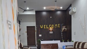 Un área de recepción moderna con un letrero que dice 'WELCOME', mostrador de recepción, zona de estar y ventilador de techo.