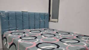 Una cama con una colcha estampada, un cabecero cubierto de plástico y una ventana con mosquitera.