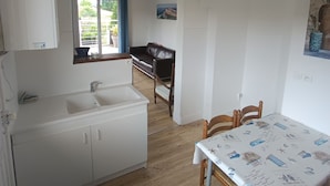 A compact kitchen with a sink, wooden cabinets, a dining table with a maritime-themed tablecloth, and a wicker ceiling light. - Villa Laurier-Rose, Swimming pool, Petanque, 16 pers, Near lake, Ocean, Town center (Parentis-en-Born)