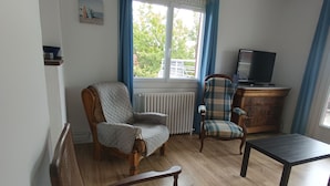 A living room with a sofa, armchair, and a television on a wooden cabinet. - Villa Laurier-Rose, Swimming pool, Petanque, 16 pers, Near lake, Ocean, Town center (Parentis-en-Born)