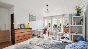 Een moderne slaapkamer met een groot bed, een houten dressoir, een zithoek met een tafel en stoelen, en een balkon met uitzicht op de stad.
