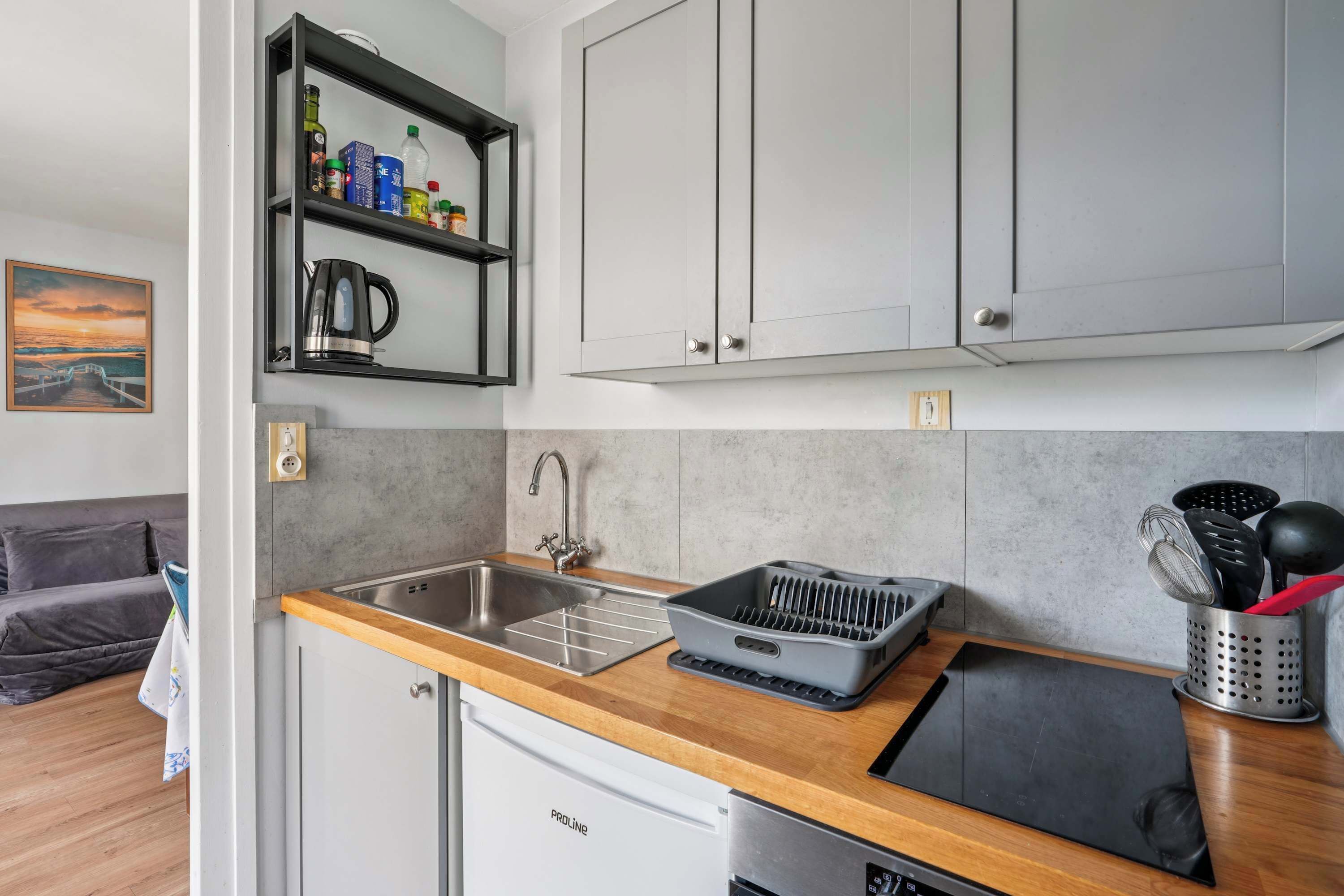 A compact kitchen with a built-in dishwasher, a coffee maker, and a shelf with various kitchen items.