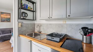 Een compacte keuken met een ingebouwde vaatwasser, een koffiezetapparaat en een plank met diverse keukenbenodigdheden.