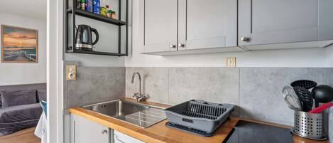 A compact kitchen with a built-in dishwasher, a coffee maker, and a shelf with various kitchen items.