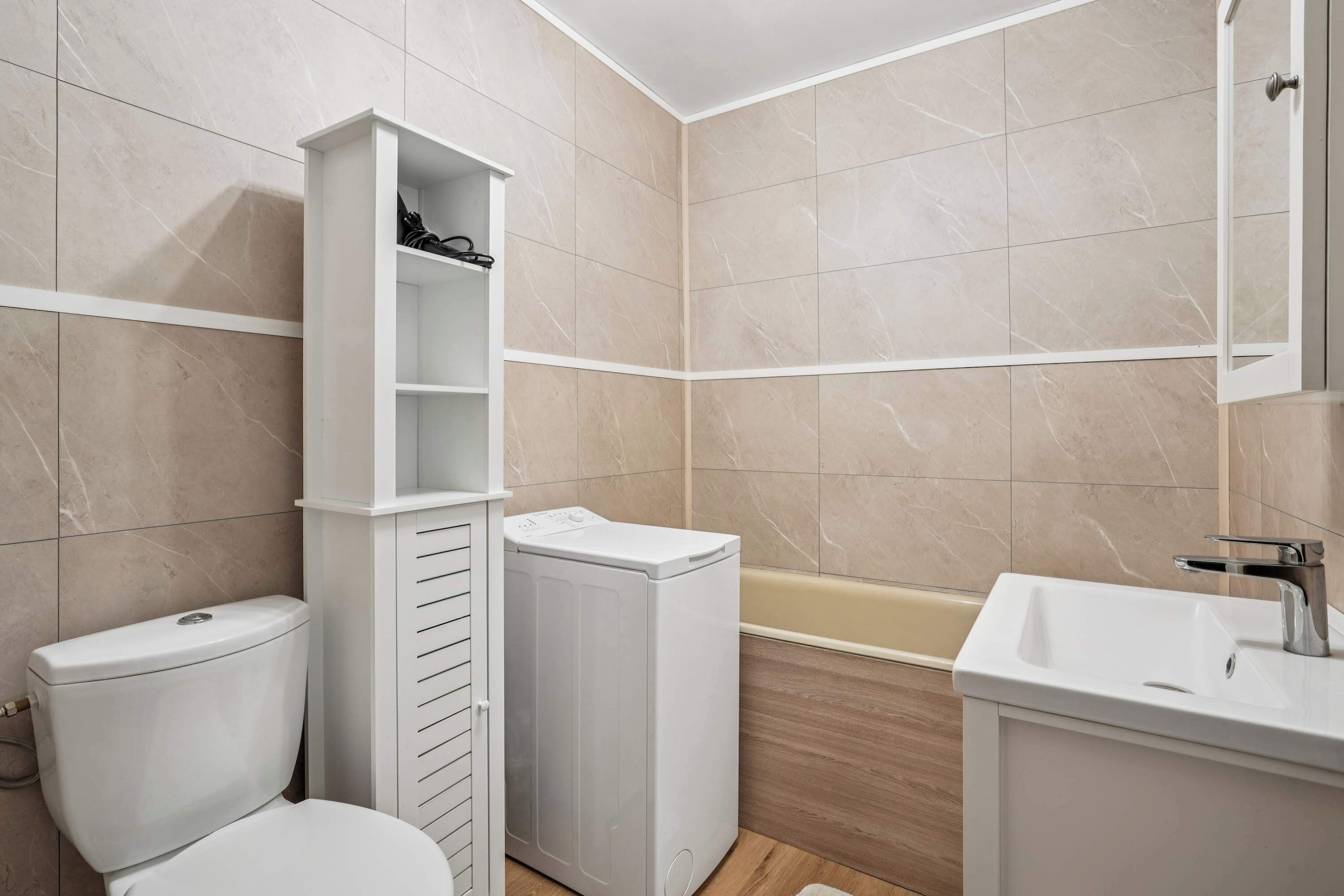 A compact bathroom with a toilet, a built-in washing machine, a bathtub, and a sink.