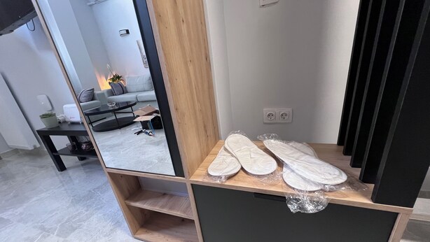 A wooden shoe rack with a mirror, a small table with a plant, and a grey sofa in the background. - Charming 2-bedroom house with WiFi, AC in fantastic Athina (Athina)