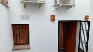 Um pátio com parede branca, janela com grade de metal, porta com portão de metal e um aparelho de ar condicionado fixado na parede.