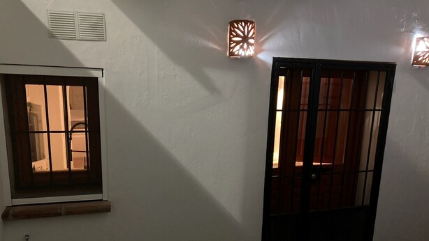 Um quarto com janela, porta e luminária fixada na parede.