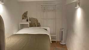 Quarto com cama, mesa de cabeceira, aquecedor fixado na parede e janela com cortina.