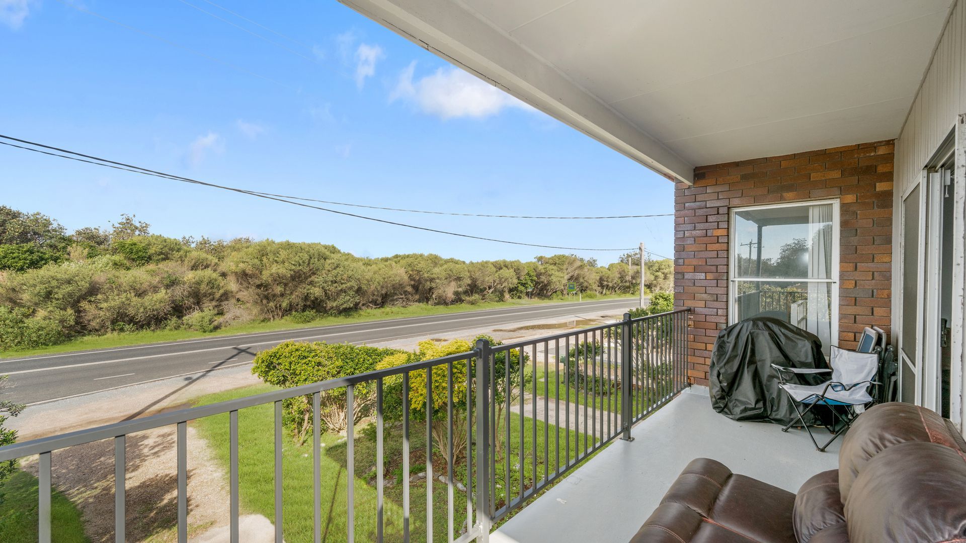 A balcony with a view of a road and greenery, a covered grill, and a seating area.
