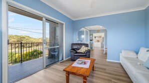 Un salon moderne avec un balcon, un fauteuil en cuir, une table basse en bois et un canapé blanc.