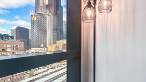 A room with a view of a city skyline through a window, a floor lamp, and a power outlet on the wall.