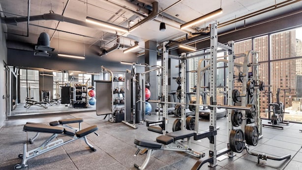 A gym with weightlifting equipment, benches, and a mirrored wall.