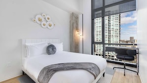 A modern bedroom with a large bed, a view of a cityscape, and a desk with a chair. - South Loop Rooftop With In and Out Parking 3 (Chicago)
