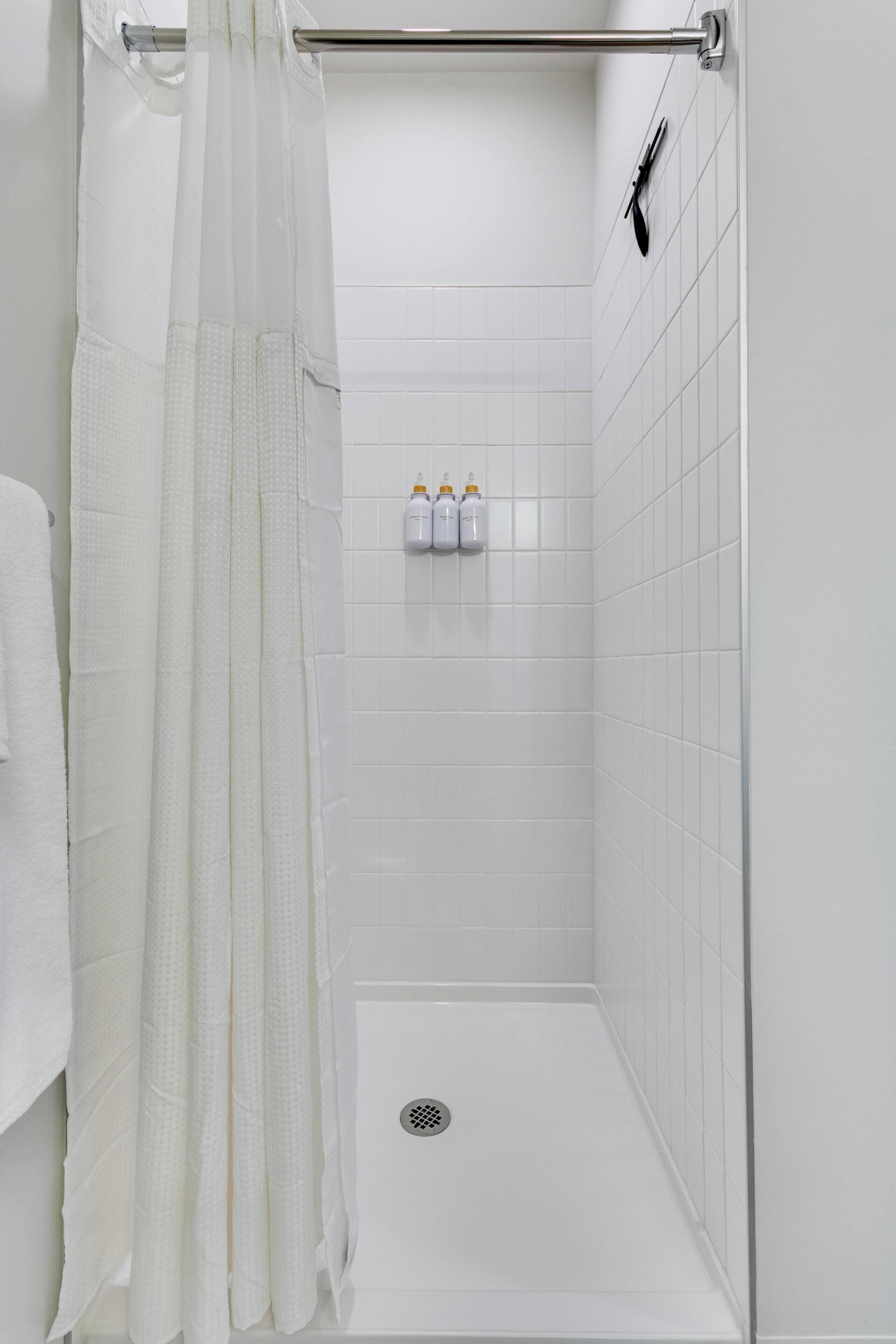 Eine weiße Dusche mit Glastür, ein weißes Handtuch und zwei Shampooflaschen an der Wand.