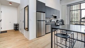 A modern kitchen with stainless steel appliances, a dining area with stools, and a large window offering a city view. - South Loop Rooftop With In and Out Parking 3 (Chicago)