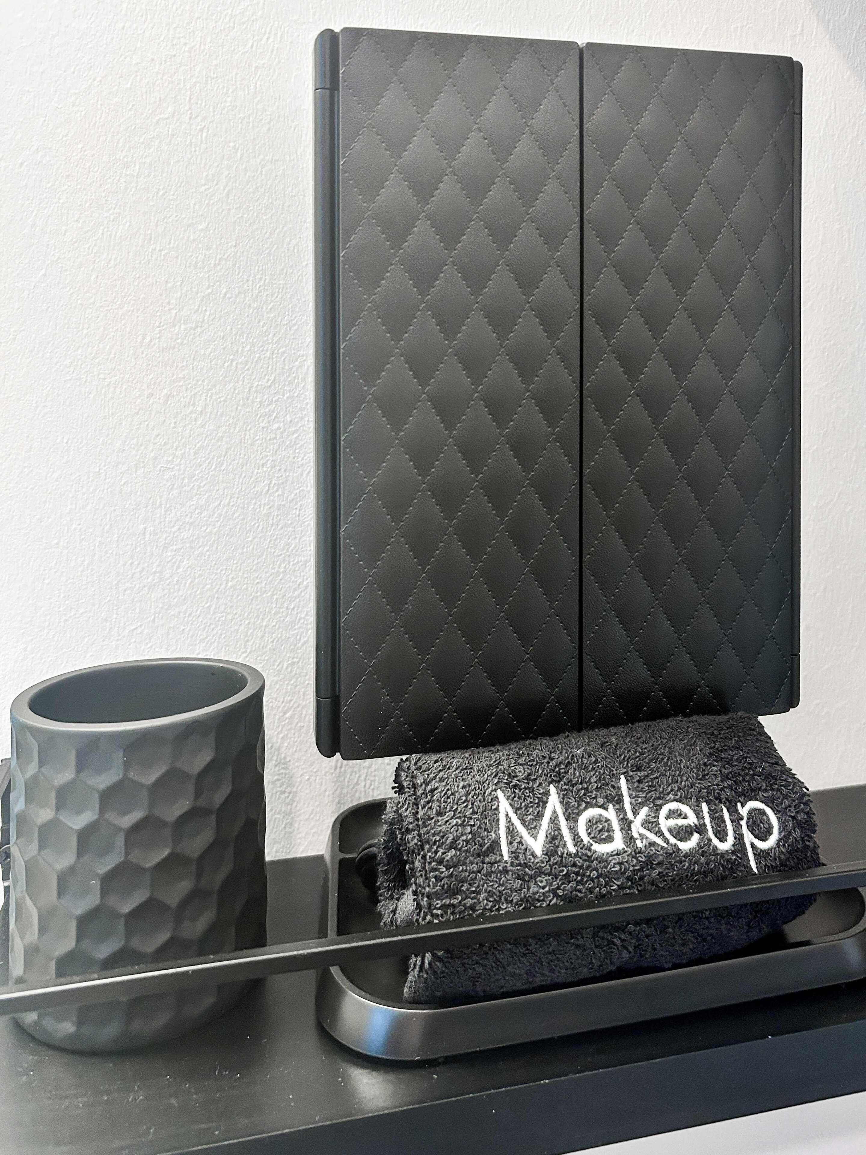 Une coiffeuse noire matelassée, avec une serviette à maquillage étiquetée « Maquillage » et une tasse texturée posée sur un plateau.