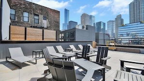 A rooftop terrace with lounge chairs and tables, overlooking a city skyline. - River North Rooftop With In and Out Parking 1 (Chicago)