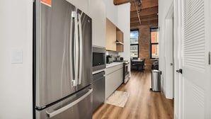 A modern kitchen with stainless steel appliances, wooden flooring, and a brick wall. - River North Rooftop With In and Out Parking 1 (Chicago)