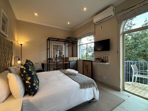 Un dormitorio con una cama grande, un escritorio con silla, un televisor montado en la pared y un balcón con barandilla.