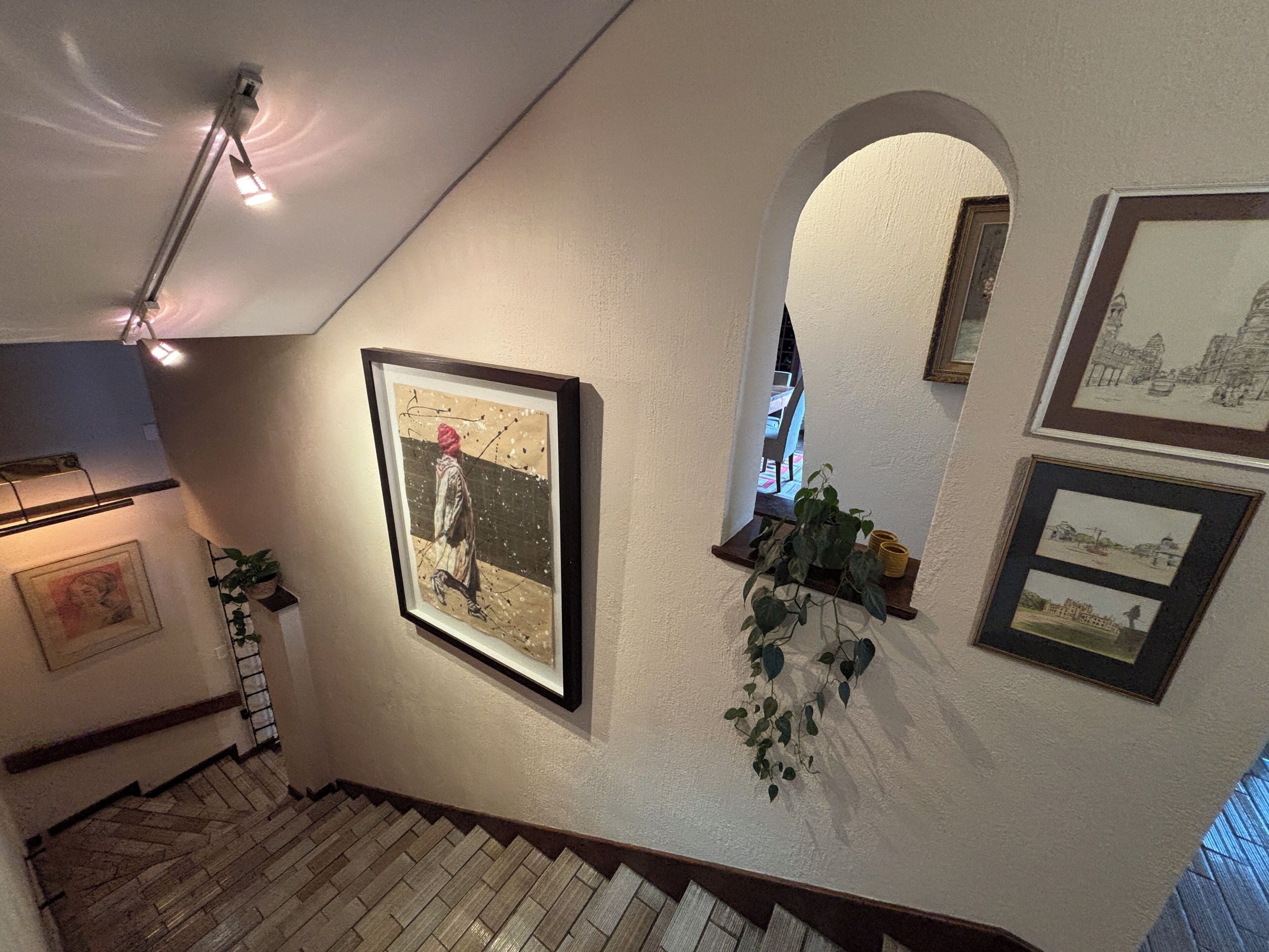 Eine Treppe mit einem Holnändergeländer, ein gerahmtes Gemälde an der Wand und ein Blumentopf.