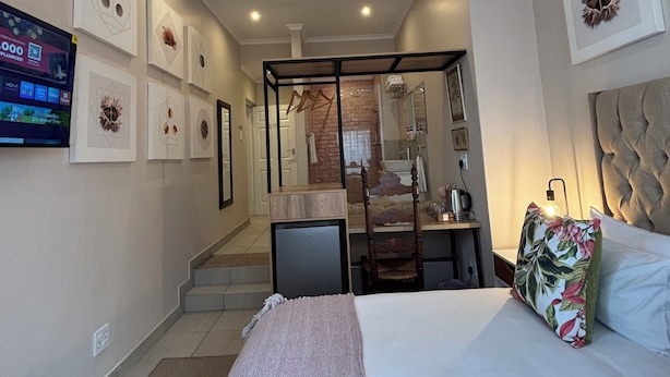 Habitación de hotel con cama, televisor, escritorio y baño visible a través de una puerta de cristal.