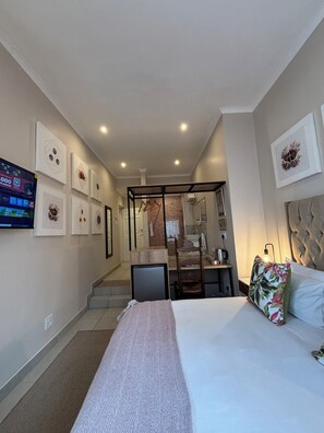 Une chambre d’hôtel équipée d’un lit, d’une télévision, d’un bureau et d’une salle de bain visible à travers une porte en verre.