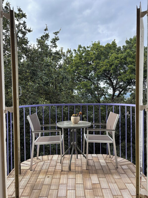Una terraza de madera con una mesa redonda y dos sillas, rodeada por una barandilla azul.