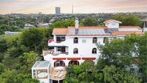 Un edificio blanco con techo de tejas rojas, paneles solares y un invernadero de cristal.