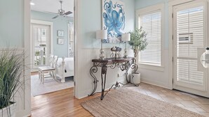 A room with a bed, a table with lamps, a ceiling fan, and a large blue artwork on the wall.