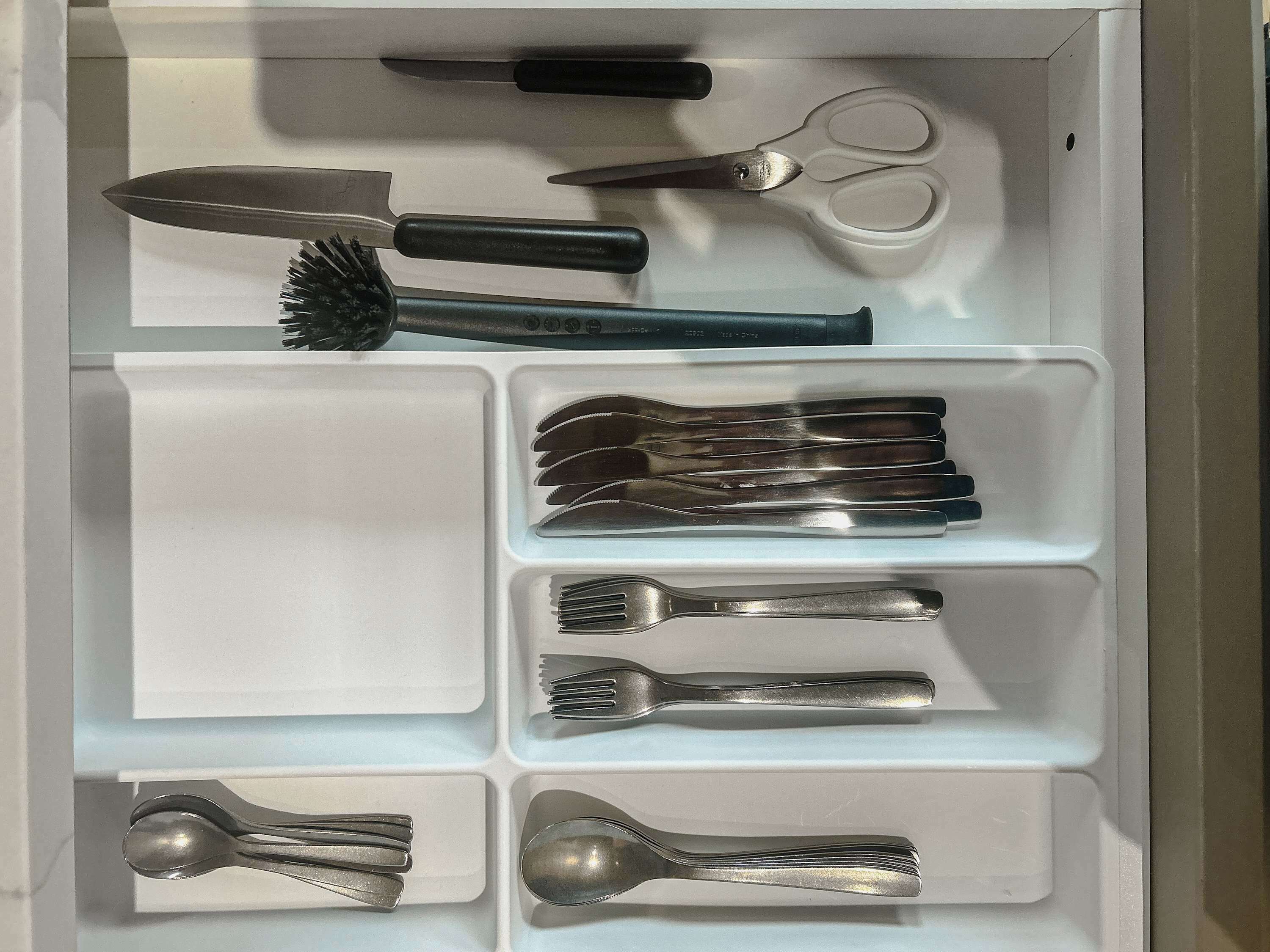A drawer with compartments containing various kitchen utensils, including a knife, scissors, and multiple forks and spoons.