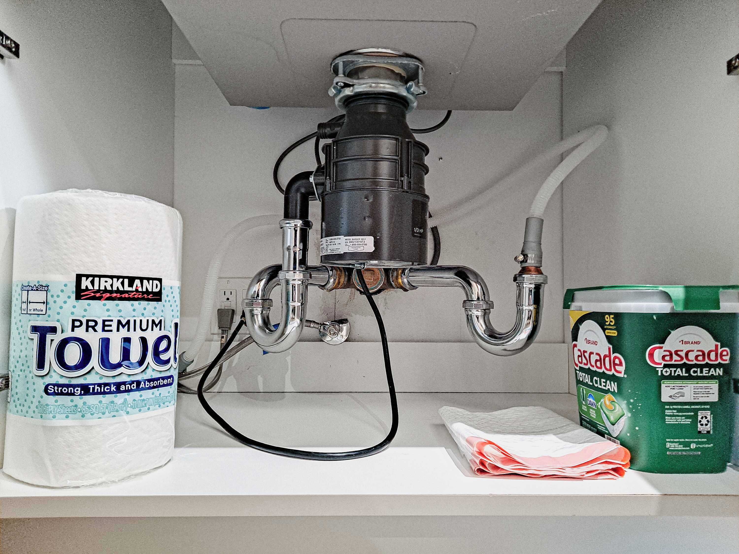 Un lavamanos con dispensador de toallas, grifo y una botella de Cascade Total Clean.