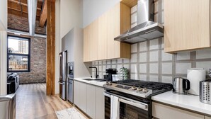 A modern kitchen with stainless steel appliances, wooden cabinets, and a large window overlooking a cityscape. - River North Rooftop With In and Out Parking 6 (Chicago)