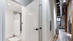 A modern interior with a hallway leading to a bathroom, featuring a white door, a shower area, and a visible kitchen area with a brick wall and stainless steel appliances. - River North Rooftop With In and Out Parking 6 (Chicago)