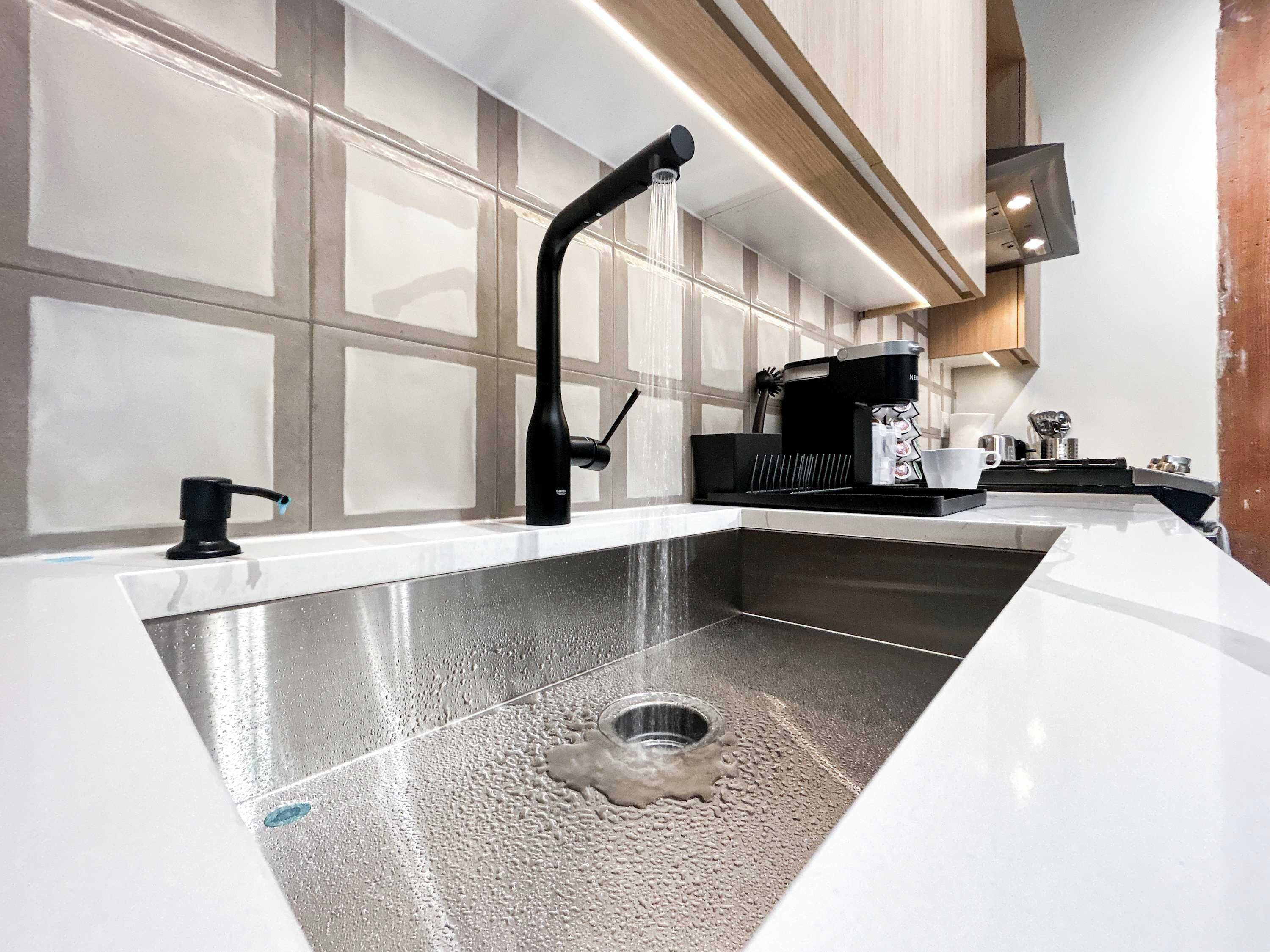 A modern kitchen with a stainless steel sink, a coffee maker, and a built-in range hood.
