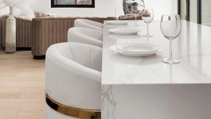 A modern dining area with a marble countertop, white upholstered chairs, and a flat-screen TV mounted on the wall. - River North Private Deck With In and Out Parking (Chicago)