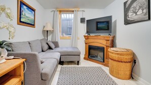 Una sala de estar con un sofá gris, chimenea, televisor y ventana con cortinas.