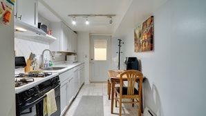 Cocina compacta con gabinetes blancos, estufa y comedor con mesa y sillas.
