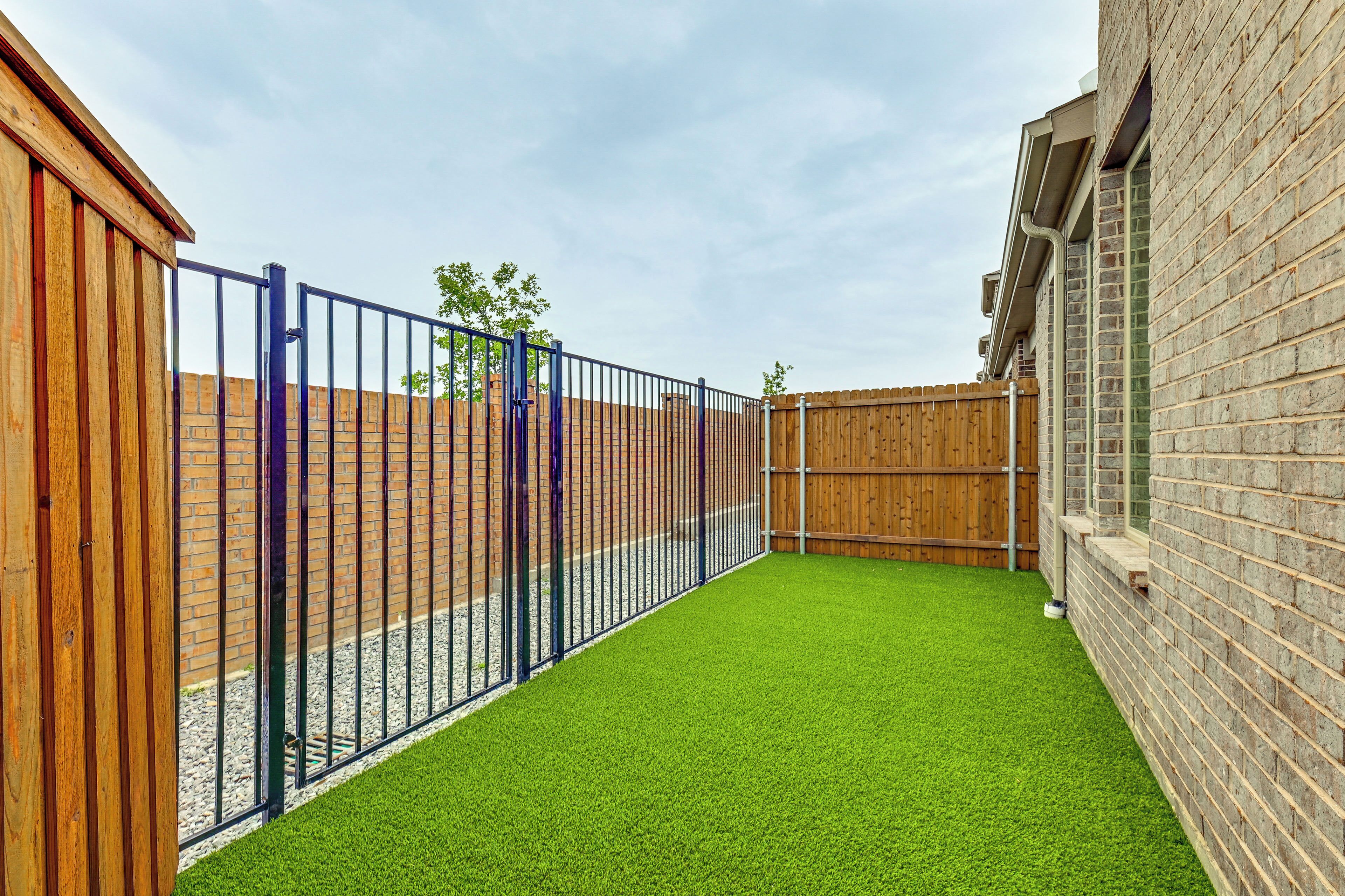 Ein eingezäunter Garten mit Kunstgrasanlage, Ziegelmauern und Holzzaun.