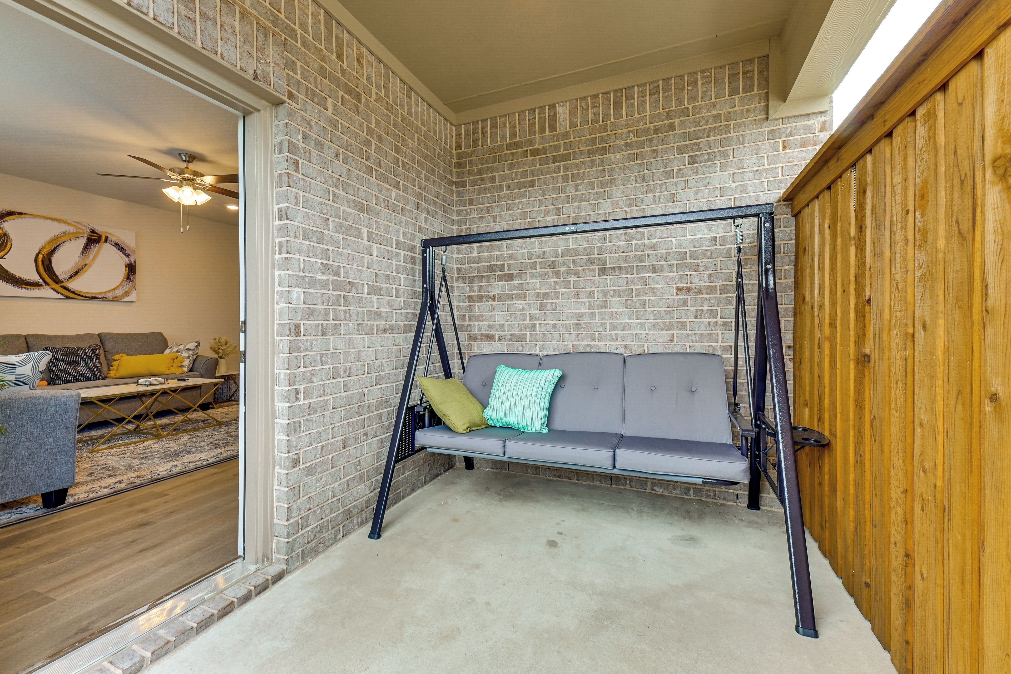 A room with a brick wall, a swing chair, a grey sofa, and a wooden door.