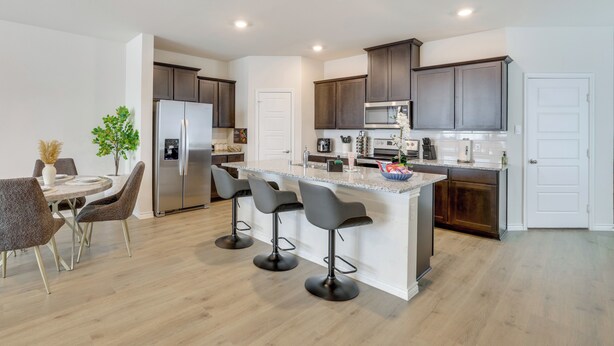 A modern kitchen with a central island, dark cabinets, stainless steel appliances, and a dining area with chairs and a table.